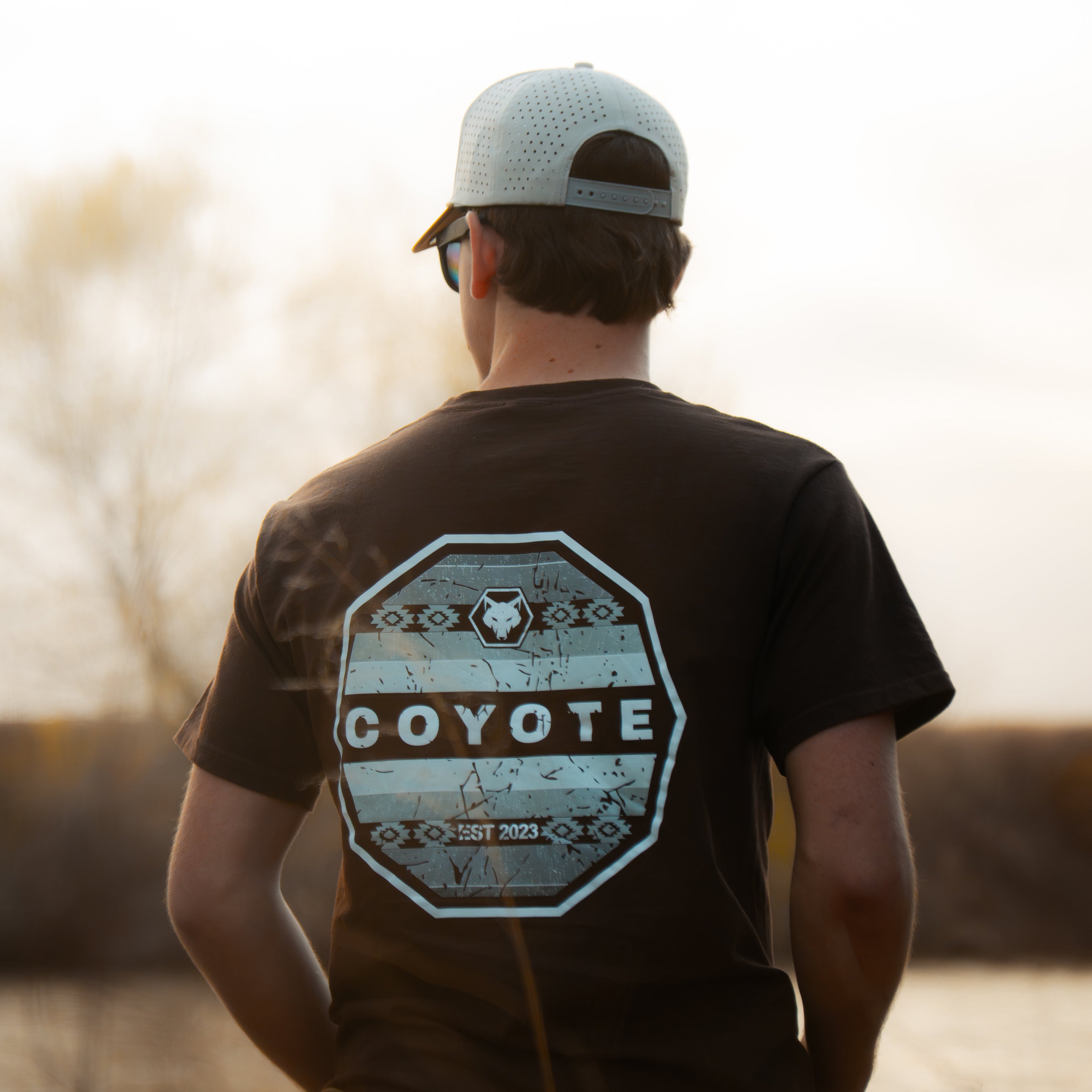 Person wearing a 'Coyote' t-shirt with a sunset or sunrise in the background