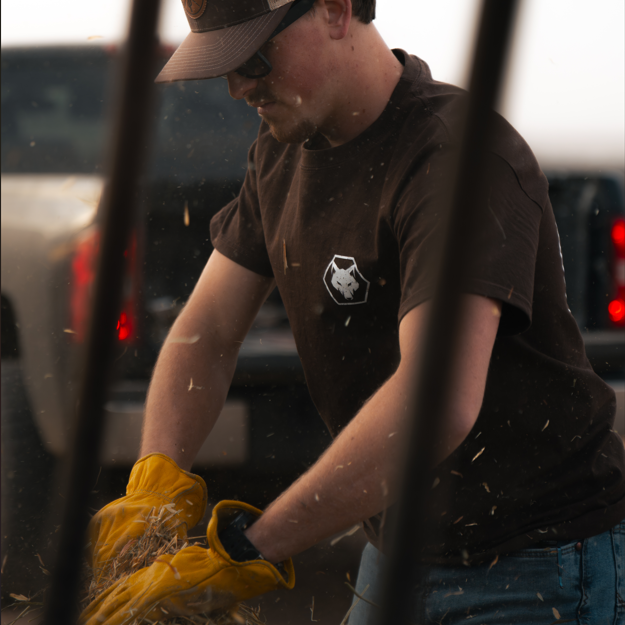 Person wearing a cap and gloves, working with hay in an outdoor setting
